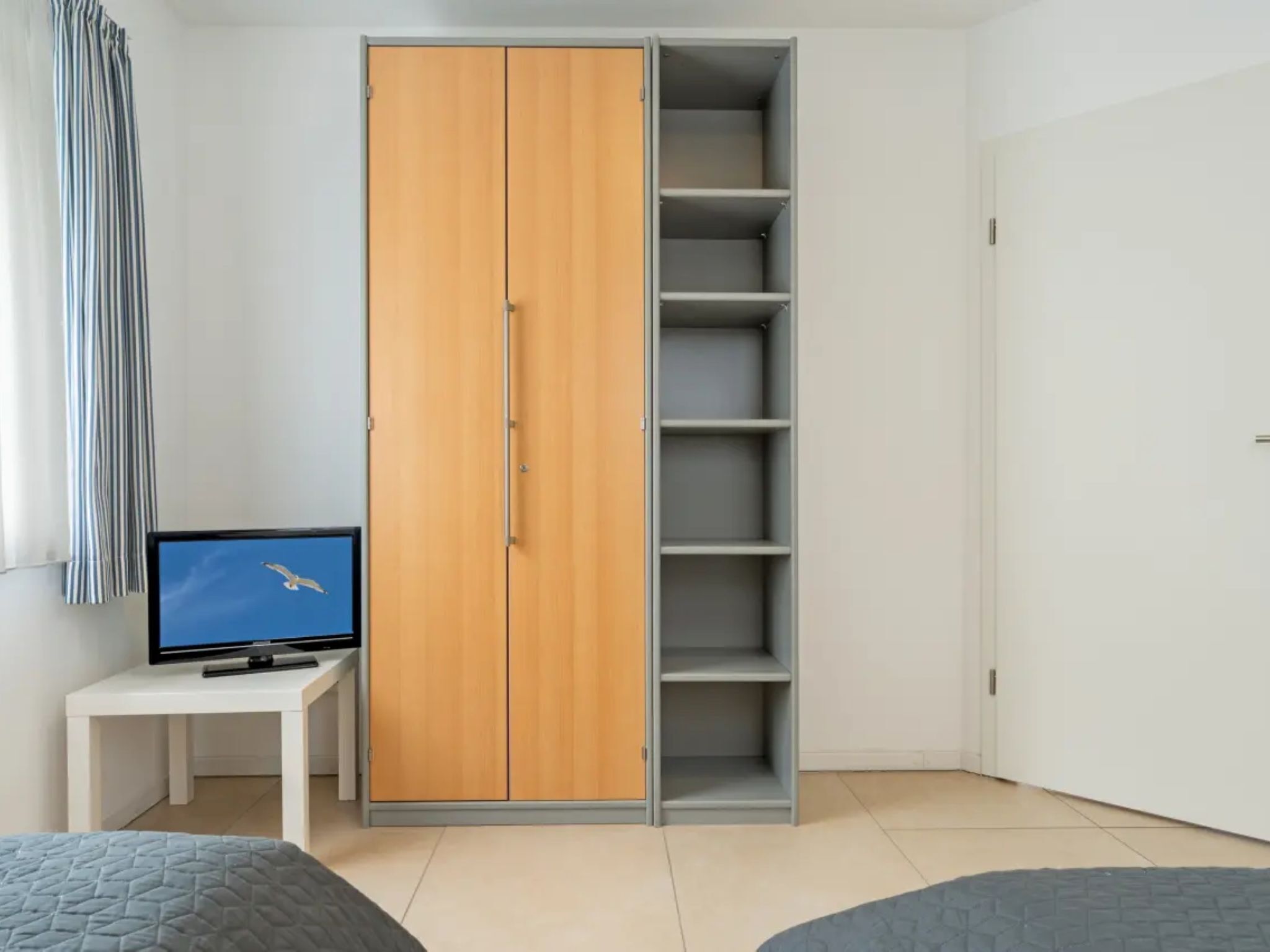A bedroom with a wardrobe, a television on a small table, and a bed.