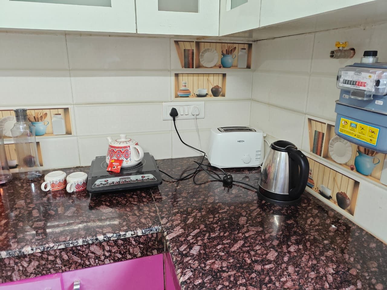 A kitchen with a granite countertop, a toaster, a kettle, and a pink cabinet.