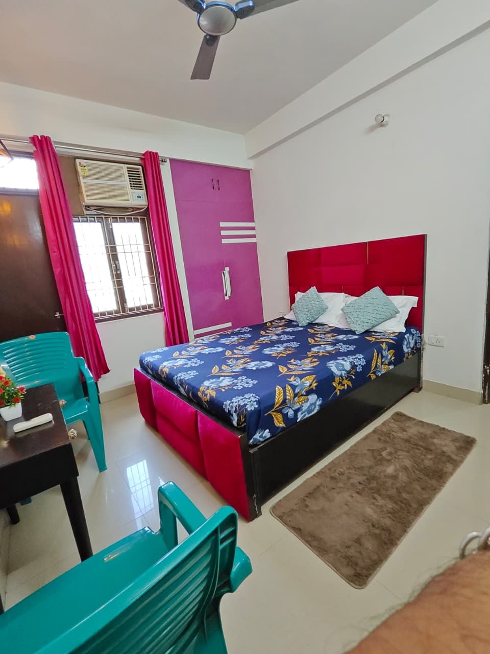 A bedroom with a bed, a desk, a chair, a window with curtains, and a ceiling fan.