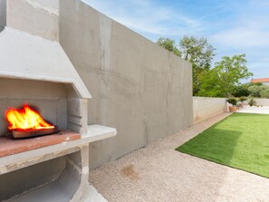 A concrete outdoor grill with a fire burning, surrounded by a grassy lawn and a low wall. - Beautiful Villa Lorna with pool by Interhome (Biograd na Moru)