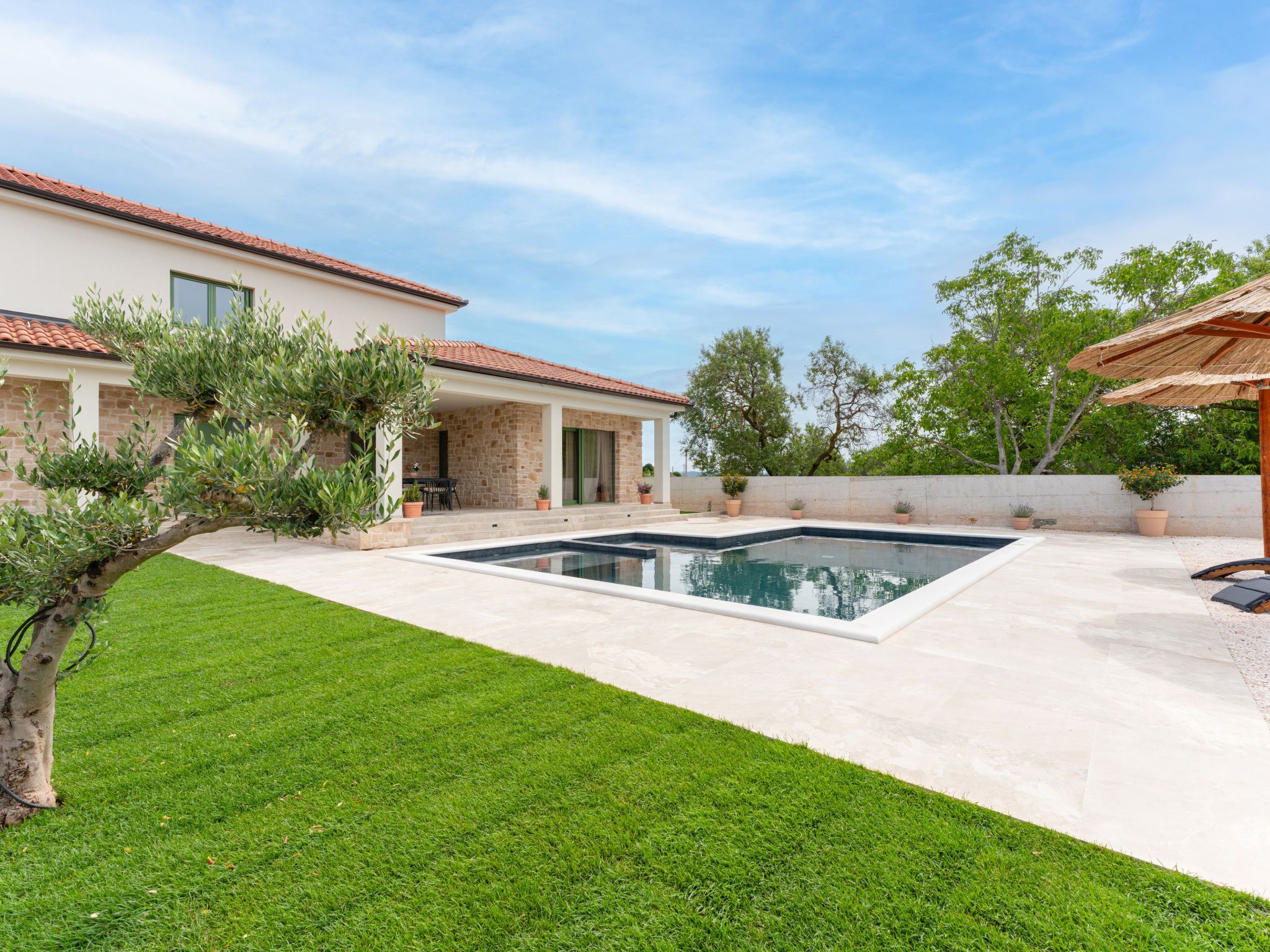 A residential property with a swimming pool, a well-maintained lawn, and a stone building with a tiled roof.