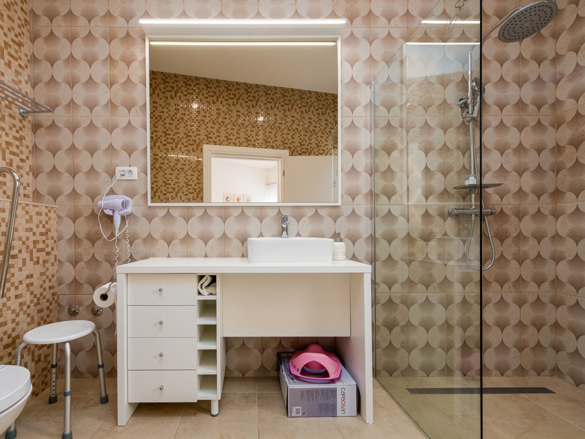 A bathroom with a white vanity, a glass shower enclosure, and patterned walls.