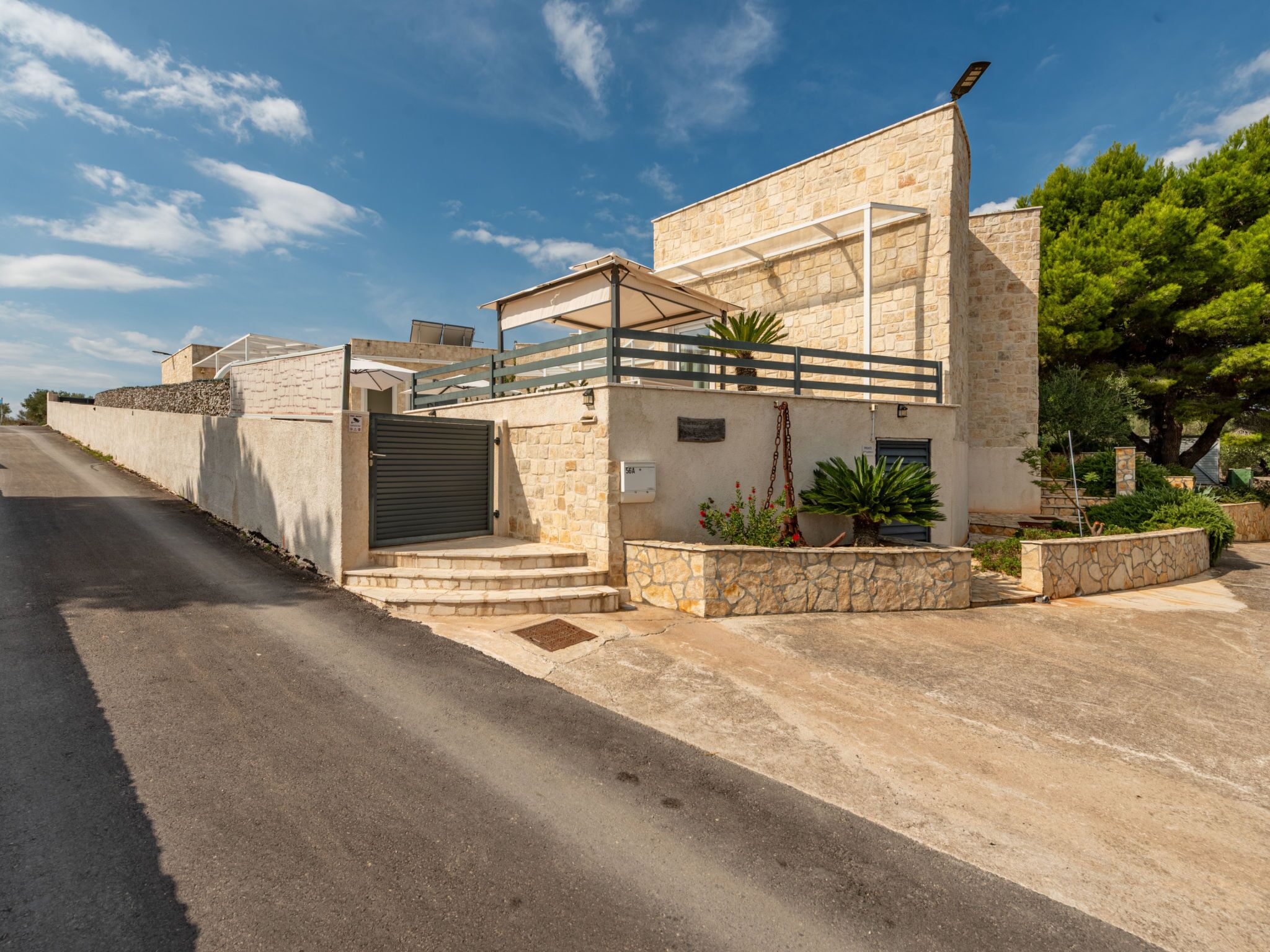 A two-story building with a stone facade, a gated entrance, and a small outdoor area with potted plants.