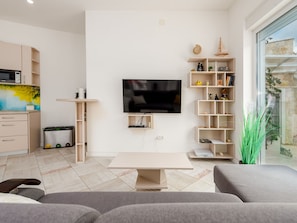 Ein modernes Wohnzimmer mit Flachbildfernseher, einer Couch, einem Couchtisch und einem Bücherregal.
