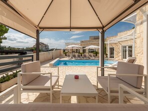 Ein überdachter Außenbereich mit Pool, Liegestühlen und einem Tisch.