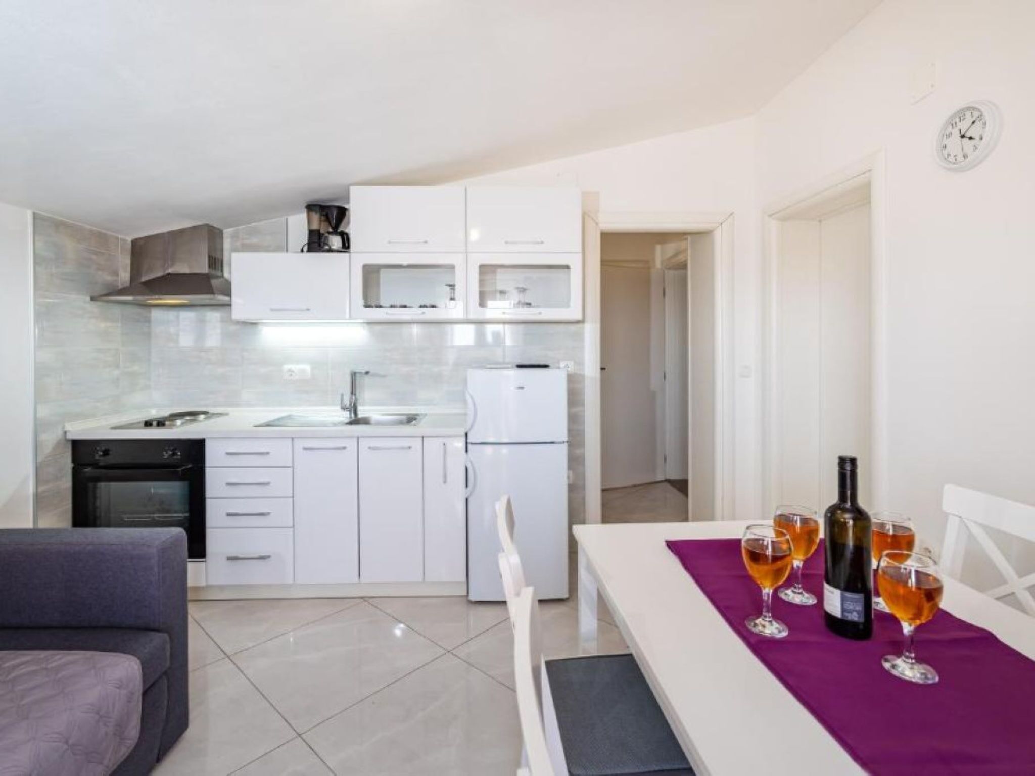 Una cucina moderna con mobili bianchi, forno integrato e frigorifero. C'è una zona pranzo con un tavolo imbandito per due, con bicchieri da vino e una bottiglia.