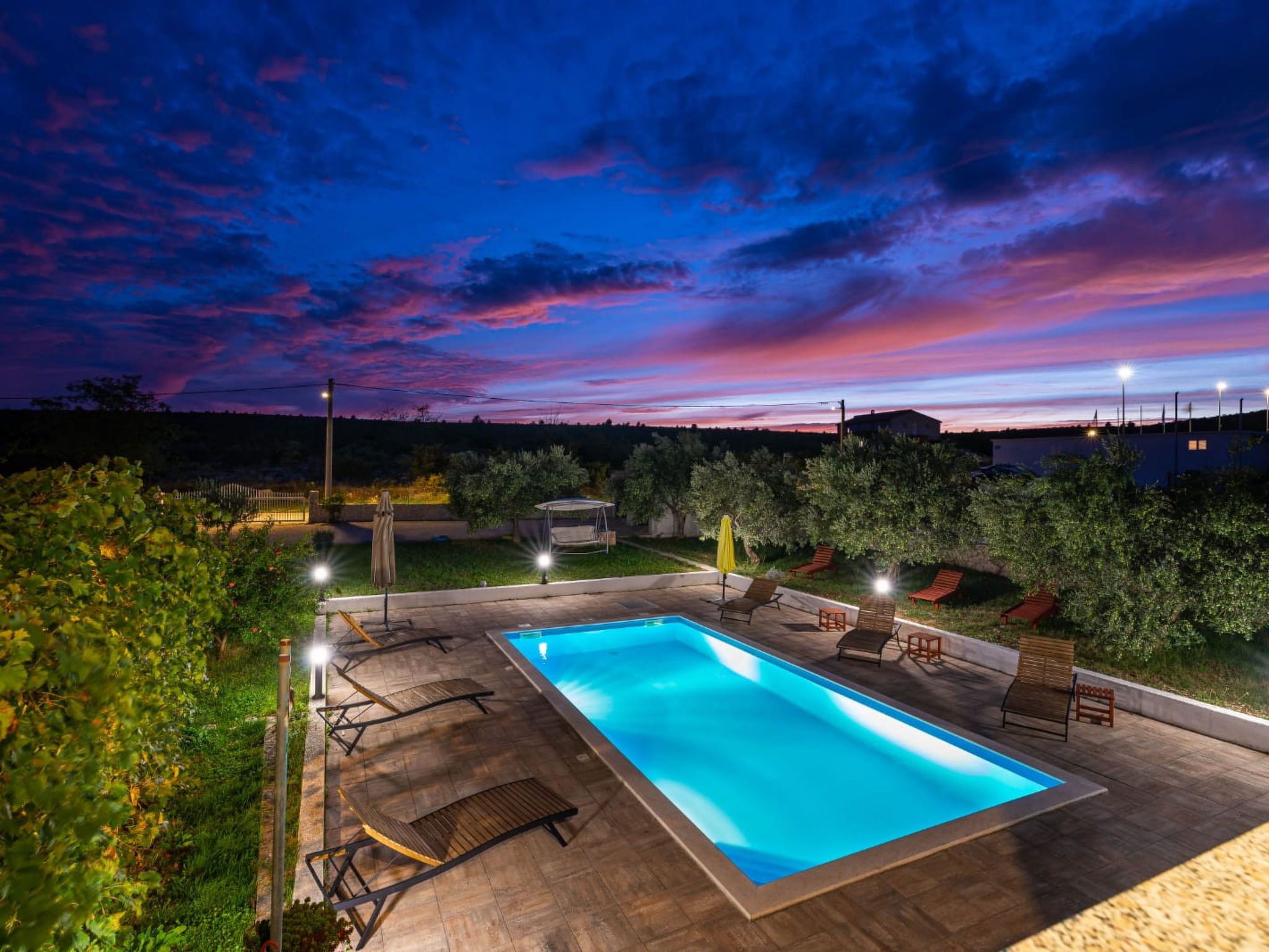 A rectangular swimming pool with a surrounding deck, equipped with lounge chairs and a sunbed.