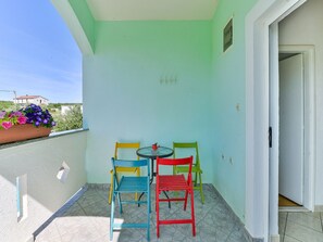 Ein kleiner Balkon mit Tisch und Stühlen, einem Blumentopf und Blick auf ein Gebäude im Hintergrund.
