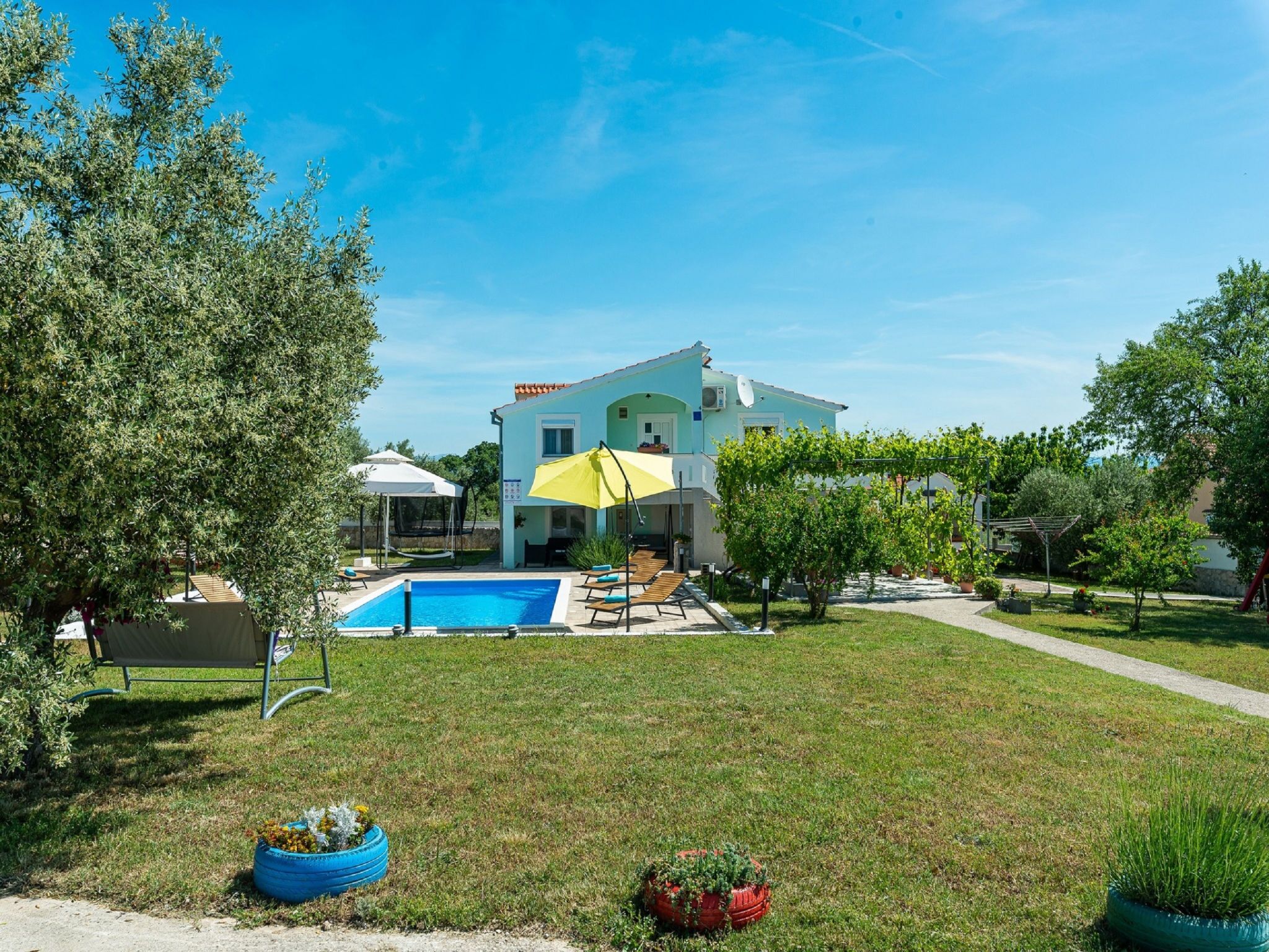 A two-story house with a swimming pool, outdoor seating, and a garden.