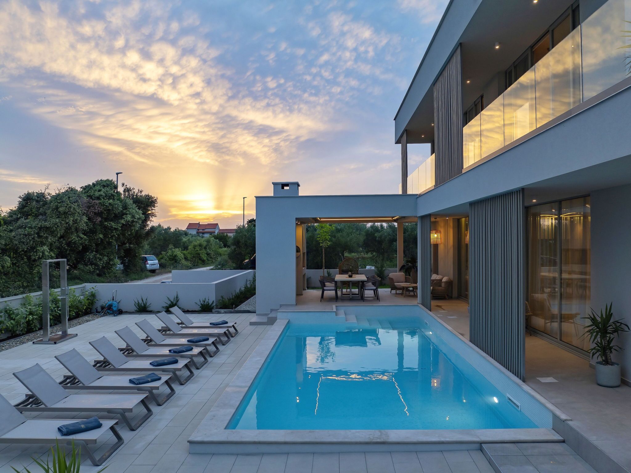 A modern outdoor pool area with lounge chairs and a dining area, surrounded by a building with large windows.