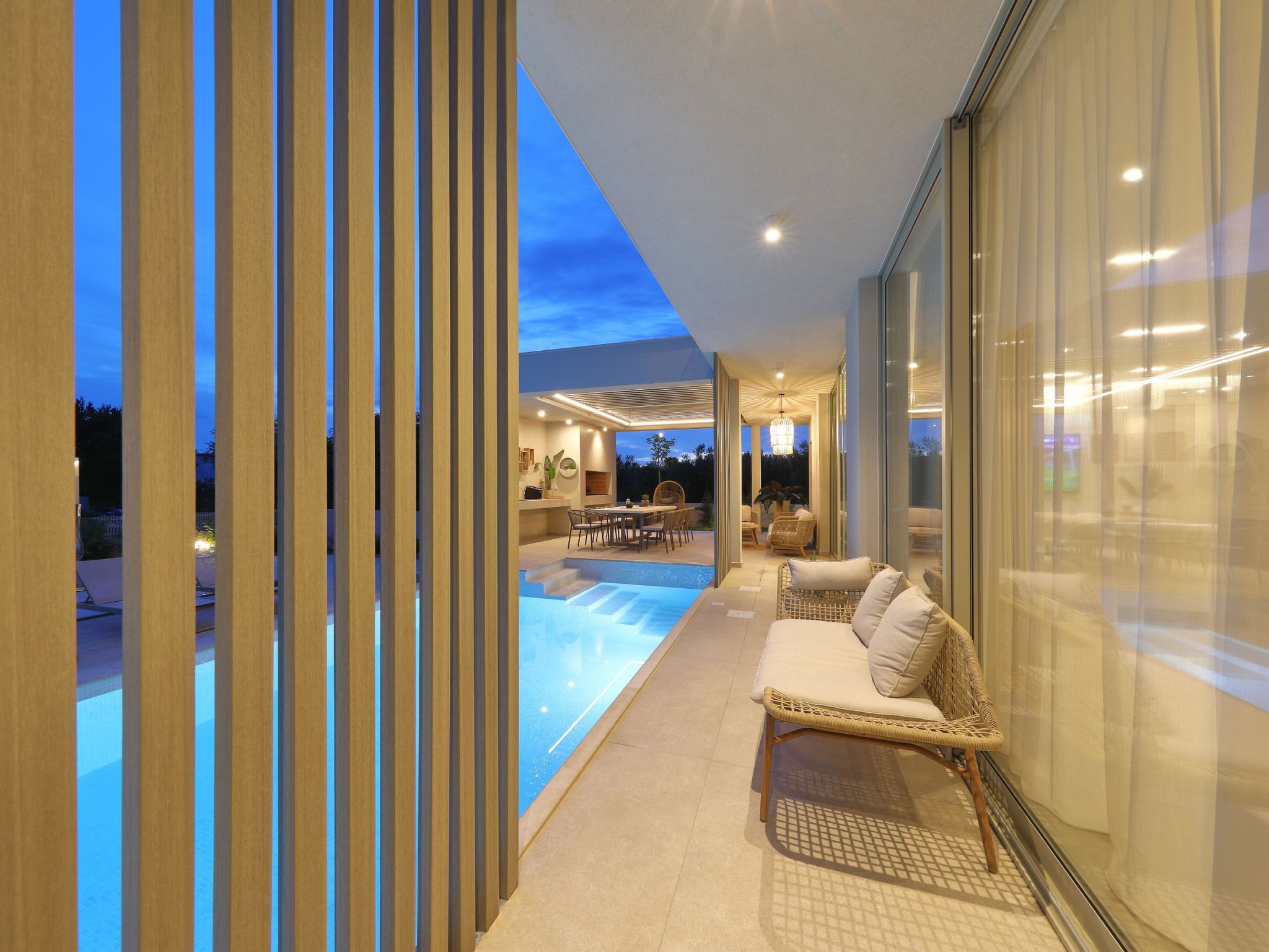 A modern indoor pool area with a lounge chair and a dining table.