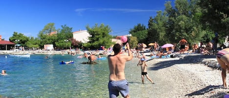 Una playa con agua cristalina, gente nadando y tomando el sol, y un bote en el agua.