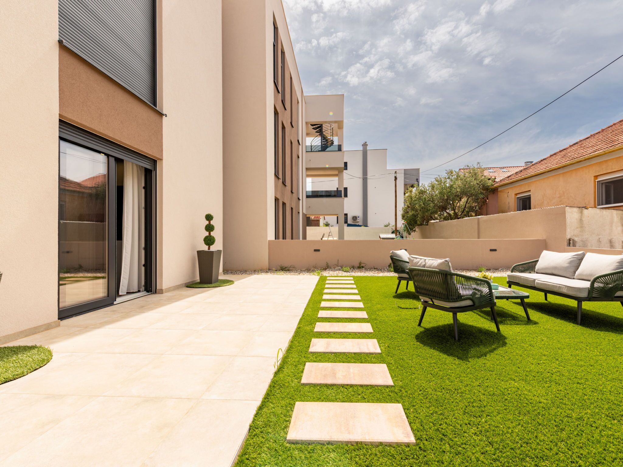 Een modern terras buiten met een duidelijke doorgang, kunstgras en tuinmeubilair.