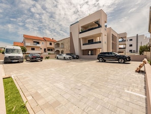 Ein Parkplatz mit mehreren Autos, einem Lieferwagen und einem Gebäude mit Balkonen und modernem Design.
