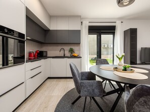 A modern kitchen with a dining area, featuring a round table, grey chairs, and a view of the outdoors. - Apartment  by Interhome (Zadar)