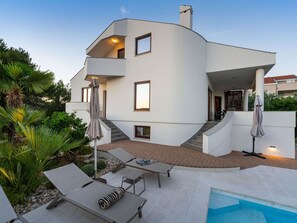 Une maison moderne à deux étages, dotée d’une piscine, d’un espace extérieur aménagé et d’un escalier menant à l’étage supérieur.
