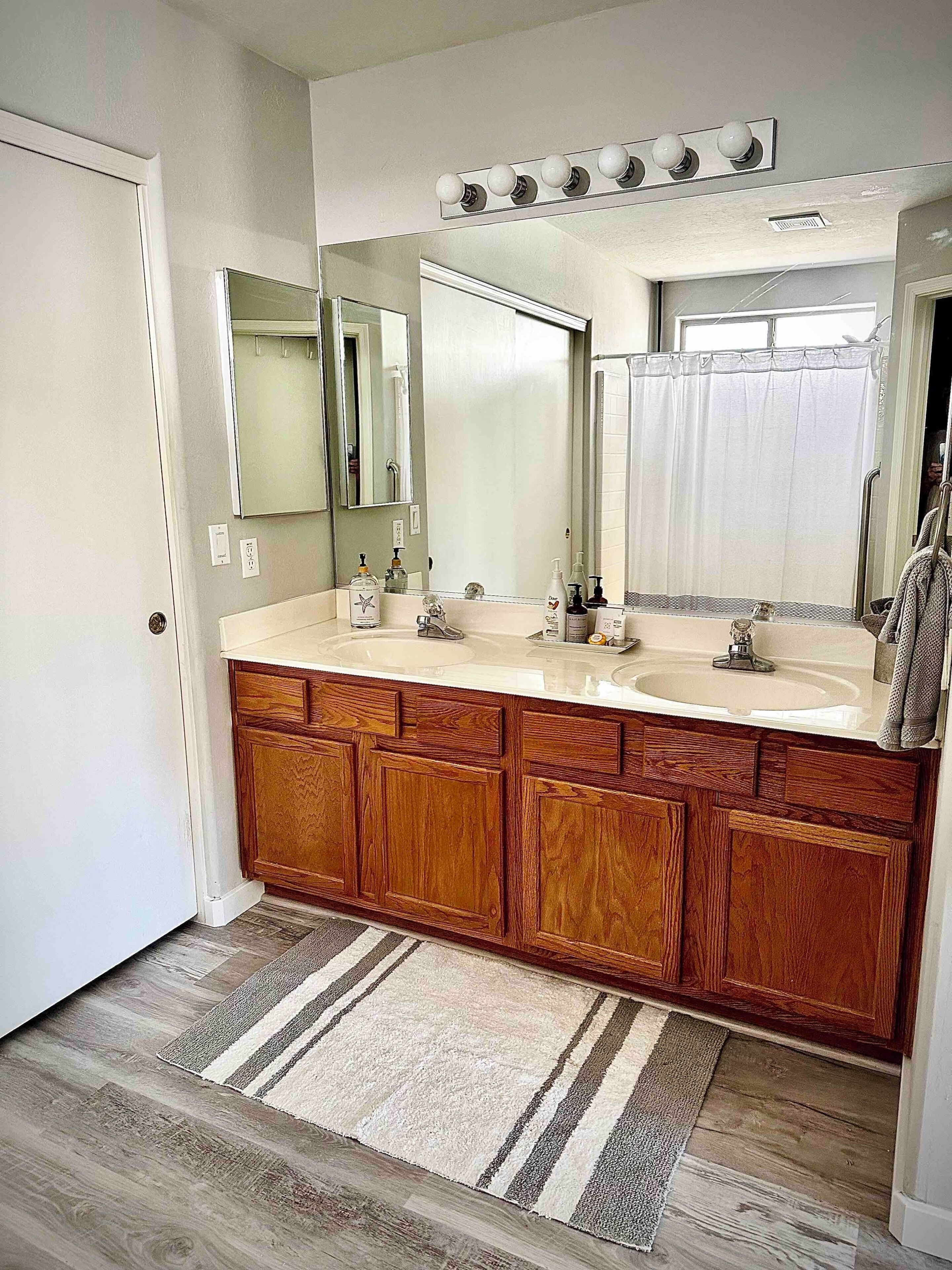 A bathroom with a double vanity, wooden cabinets, a large mirror, and a striped rug.
