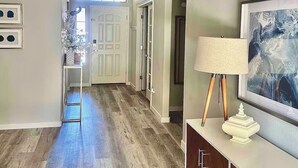A hallway with a wooden floor, a white door, a white console table with a lamp, and a framed picture on the wall. - Surprise tropical oasis with private heated pool! (Surprise)