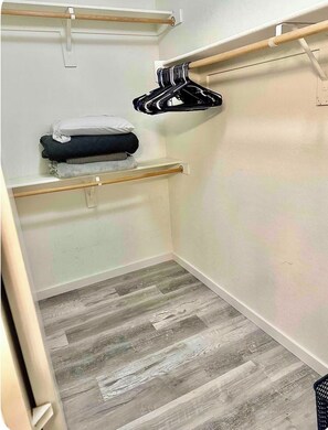 Ein kleiner, abgeschlossener Schrank mit Holzboden, einer Kleiderstange und einem Fach mit gefalteter Kleidung.