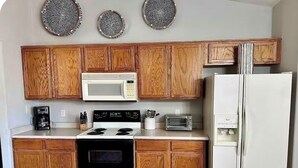 A kitchen with wooden cabinets, a microwave, a stove, a refrigerator, and a toaster. - Surprise tropical oasis with private heated pool! (Surprise)
