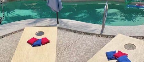 Deux chaises longues en bois, avec des serviettes rouges et bleues, une piscine et un palmier en arrière-plan.