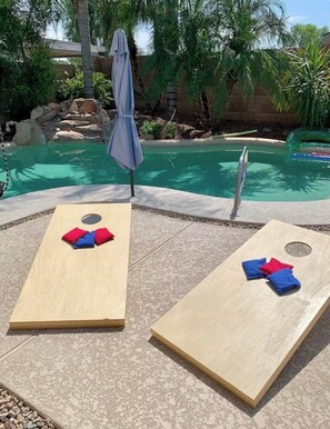 Dos tumbonas de madera con toallas rojas y azules, una piscina y una palmera al fondo.