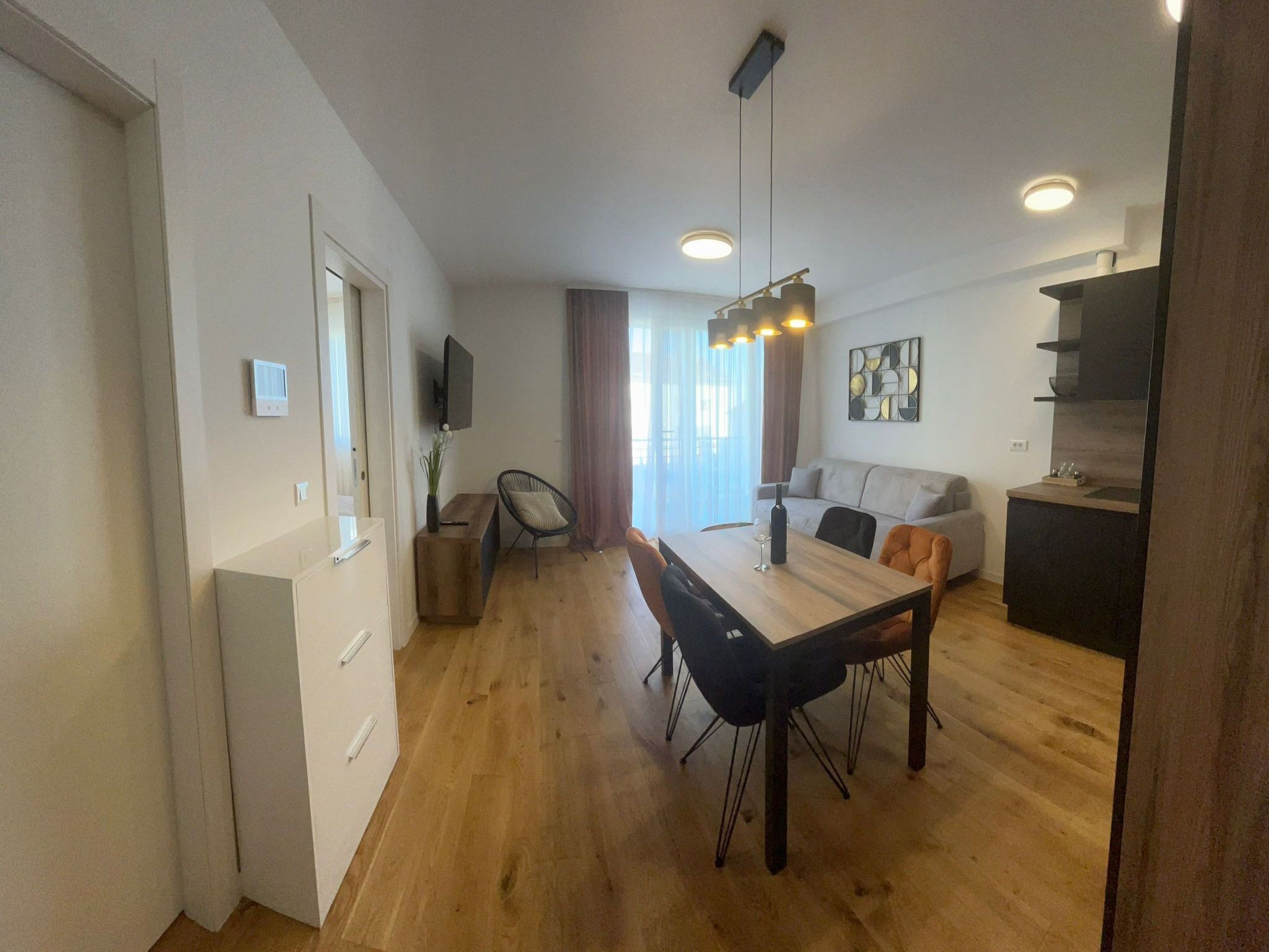 A modern living room with a dining table, sofa, and a TV mounted on the wall.