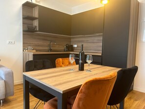 A modern kitchen with a wooden countertop and black cabinets. There is a dining table with two chairs, one orange and one black. Two wine glasses and a bottle are on the table. - Apartment Gold Shine by Interhome (Zadar)