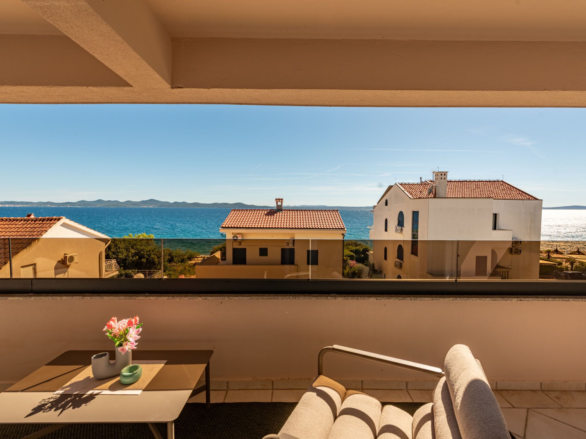 A balcony with a view of the sea, a table with a vase of flowers, and a chair.