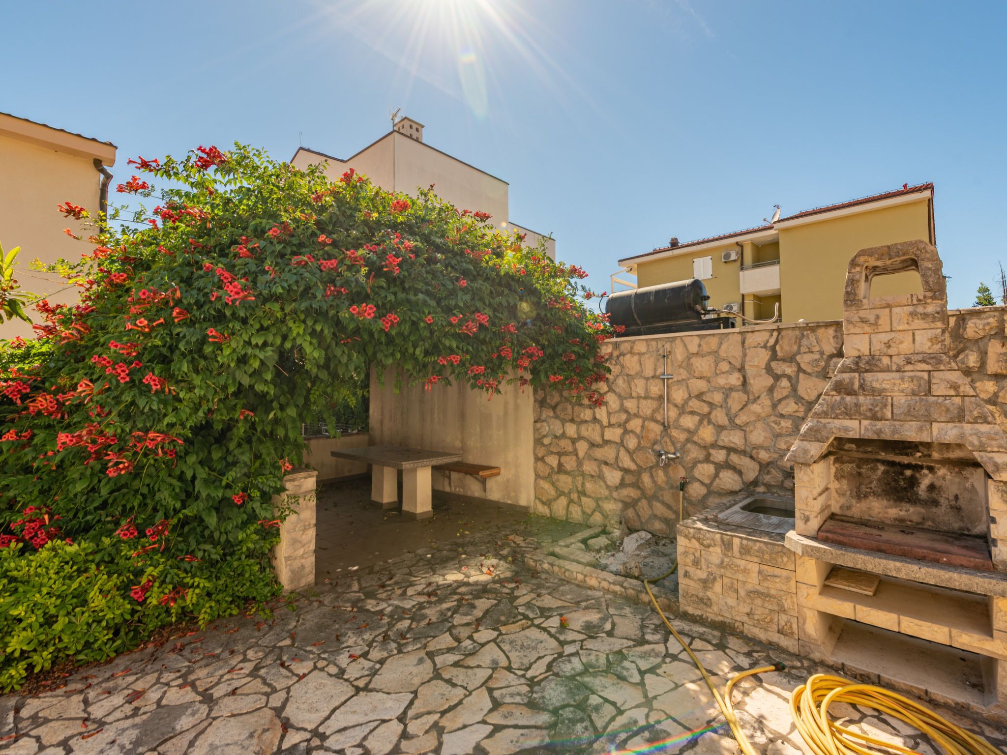 A stone patio with a stone wall, a barbecue grill, and a bench.
