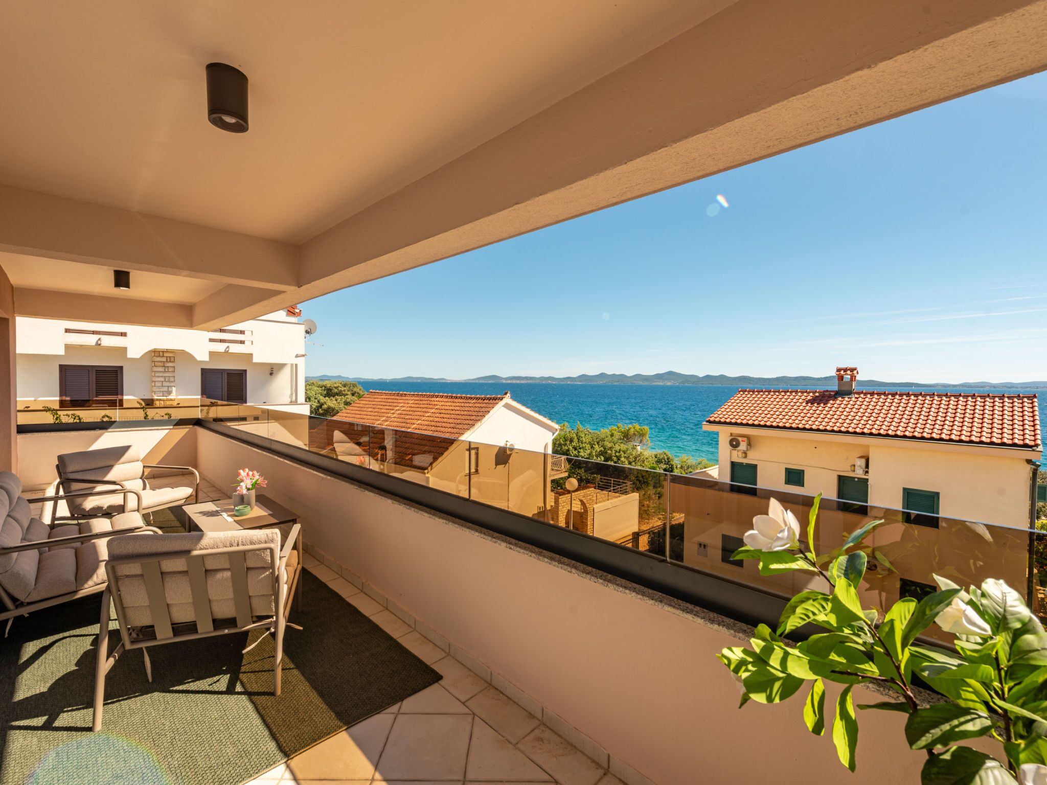 A balcony with a view of the sea, outdoor furniture, and a clear sky.