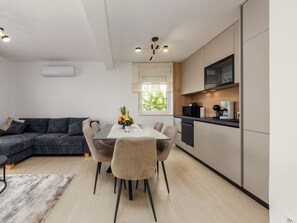 A modern kitchen with a dining area, a sofa, and a window with a view of greenery. - Apartment  by Interhome (Zadar/Kožino)
