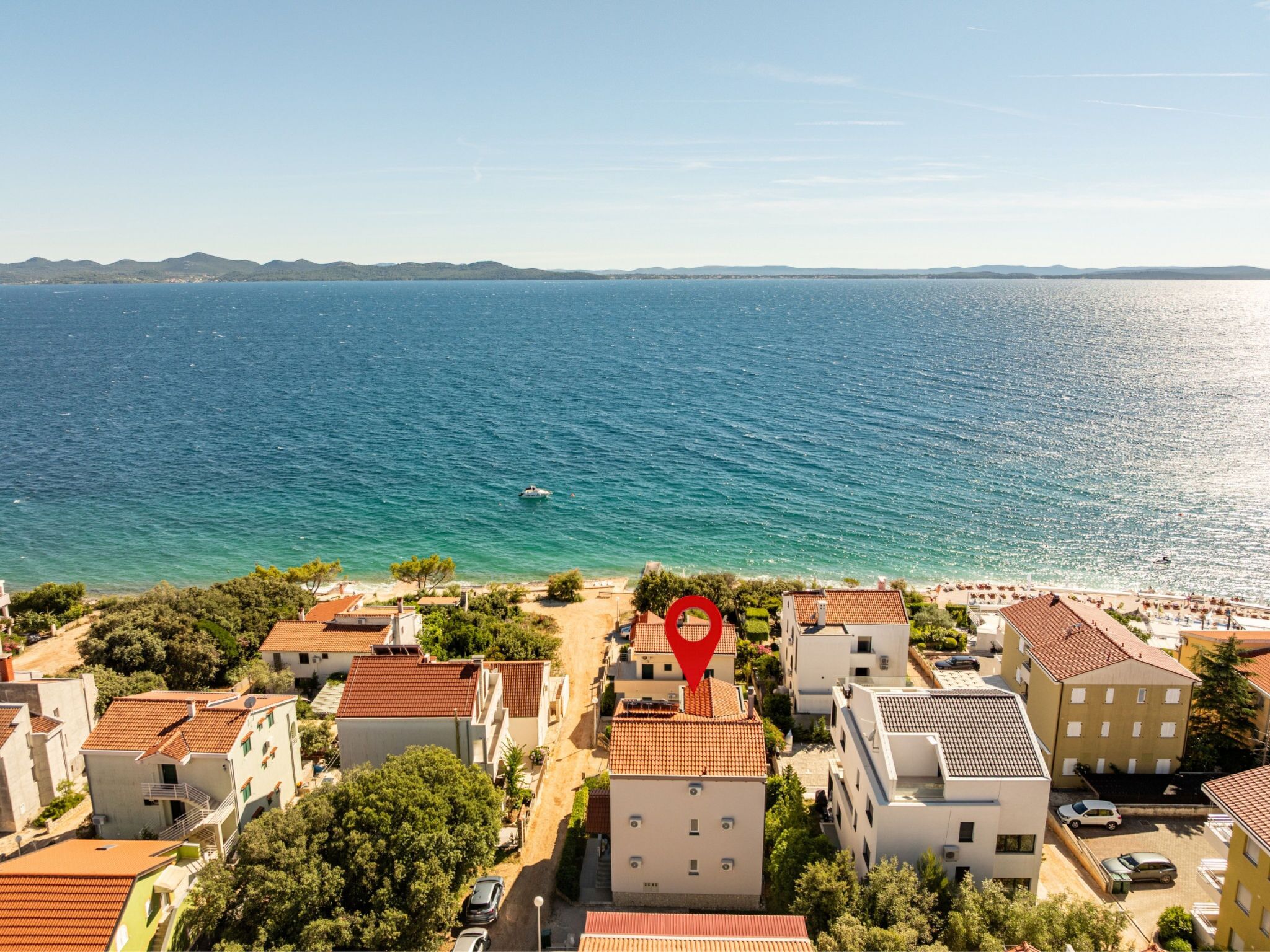 A coastal town with buildings, a clear view of the sea, and a red location marker.