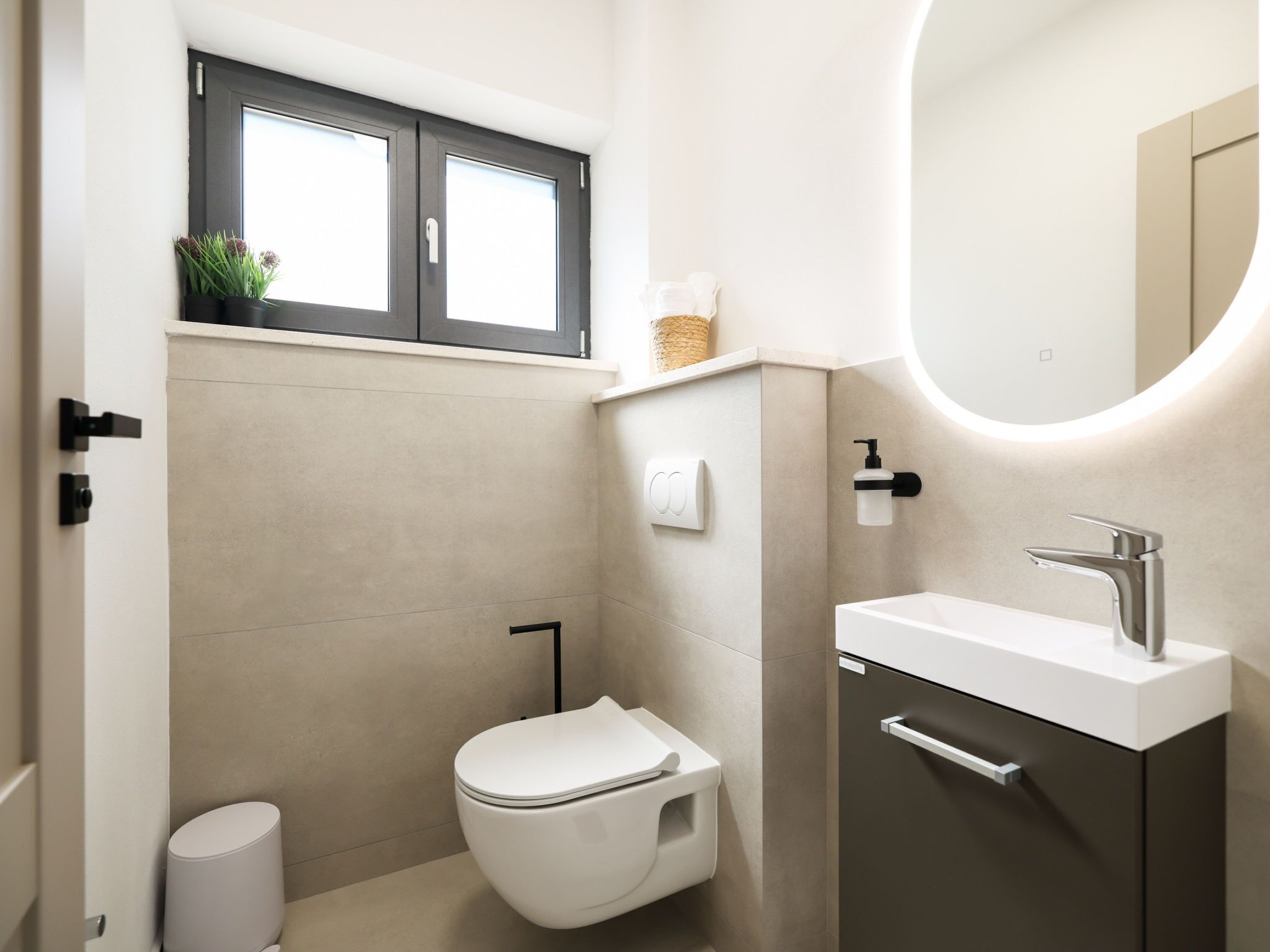 Une salle de bain moderne équipée de toilettes, d’un lavabo et d’une fenêtre située au-dessus des toilettes.