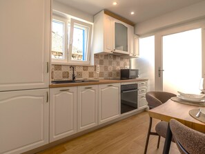 A kitchen with white cabinetry, a microwave, an oven, and a dining area with a table and chairs. - Holiday House Blažov Dvor with jacuzzi by Interhome (Zaton)