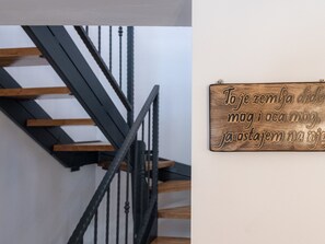 Une enseigne en bois avec du texte, fixée à un mur, un escalier avec des rampes noires et des marches en bois.