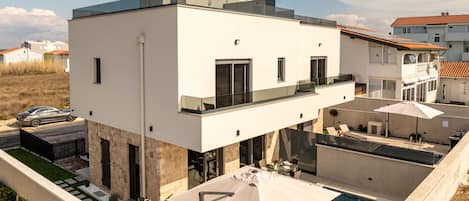A modern two-story house with a rooftop pool, outdoor seating, and a car parked nearby.