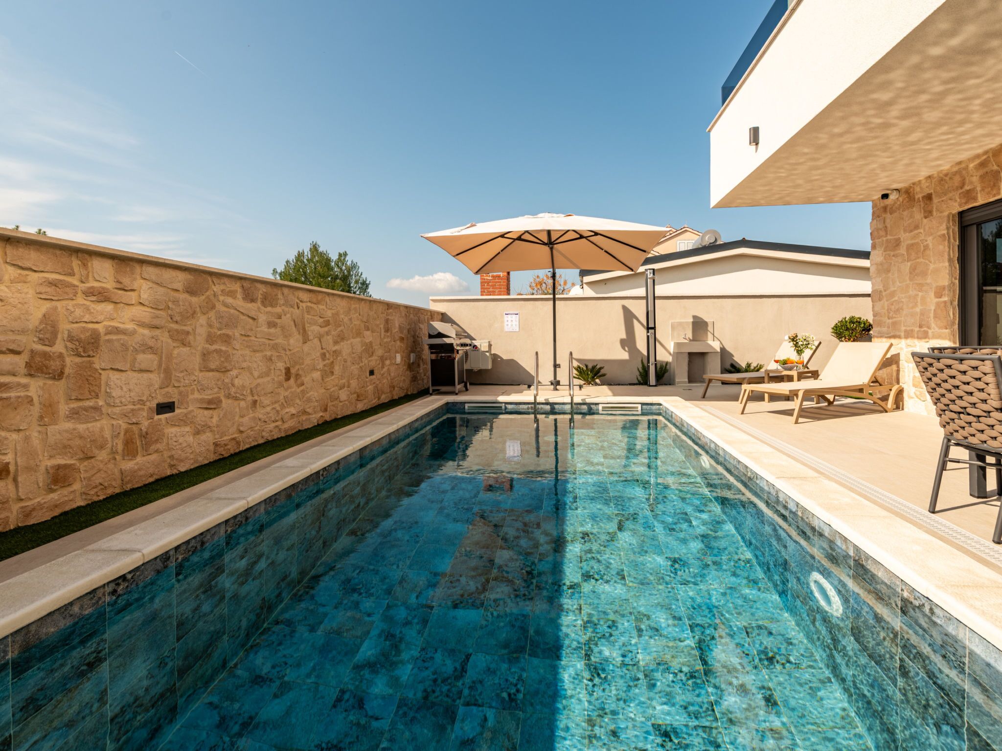Ein Swimmingpool mit Steinmauer, Grillplatz und Sitzgelegenheiten im Freien.