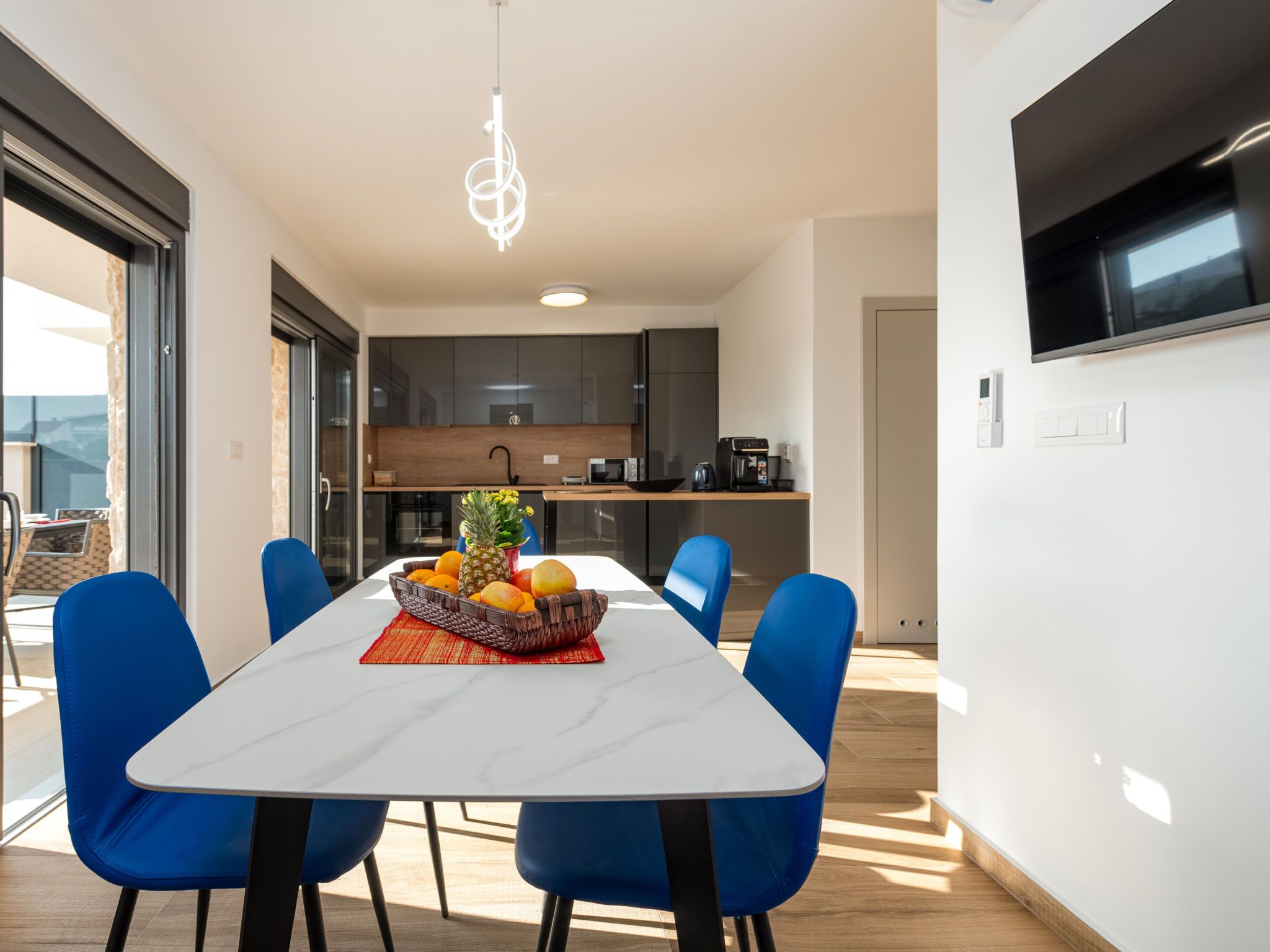 A modern dining area with a white table, blue chairs, and a fruit bowl on the table.