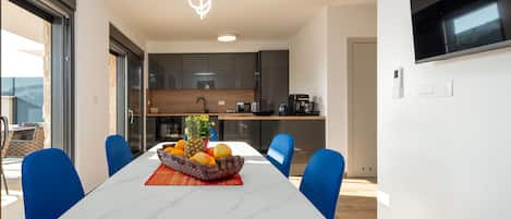 A modern dining area with a white table, blue chairs, and a fruit bowl on the table.