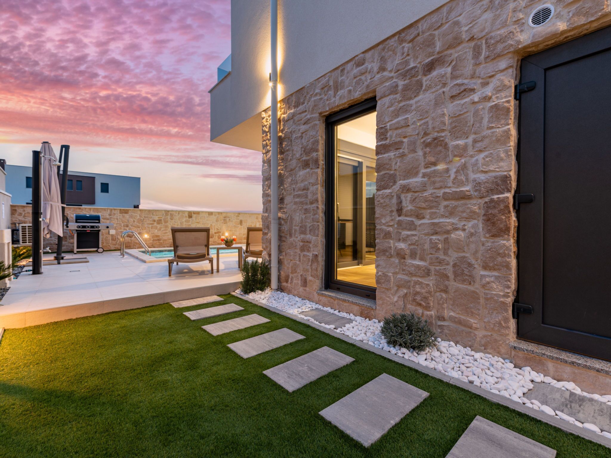 A modern house with a stone facade, a pool, and outdoor furniture.