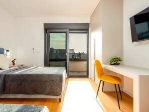 Ein modernes Schlafzimmer mit Bett, Schreibtisch, Stuhl und einem an der Wand befestigten Fernseher.