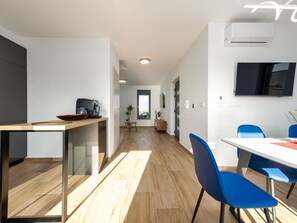 Eine moderne Küche mit Kaffeemaschine, ein Essbereich mit blauen Stühlen und ein an der Wand befestigter Fernseher.