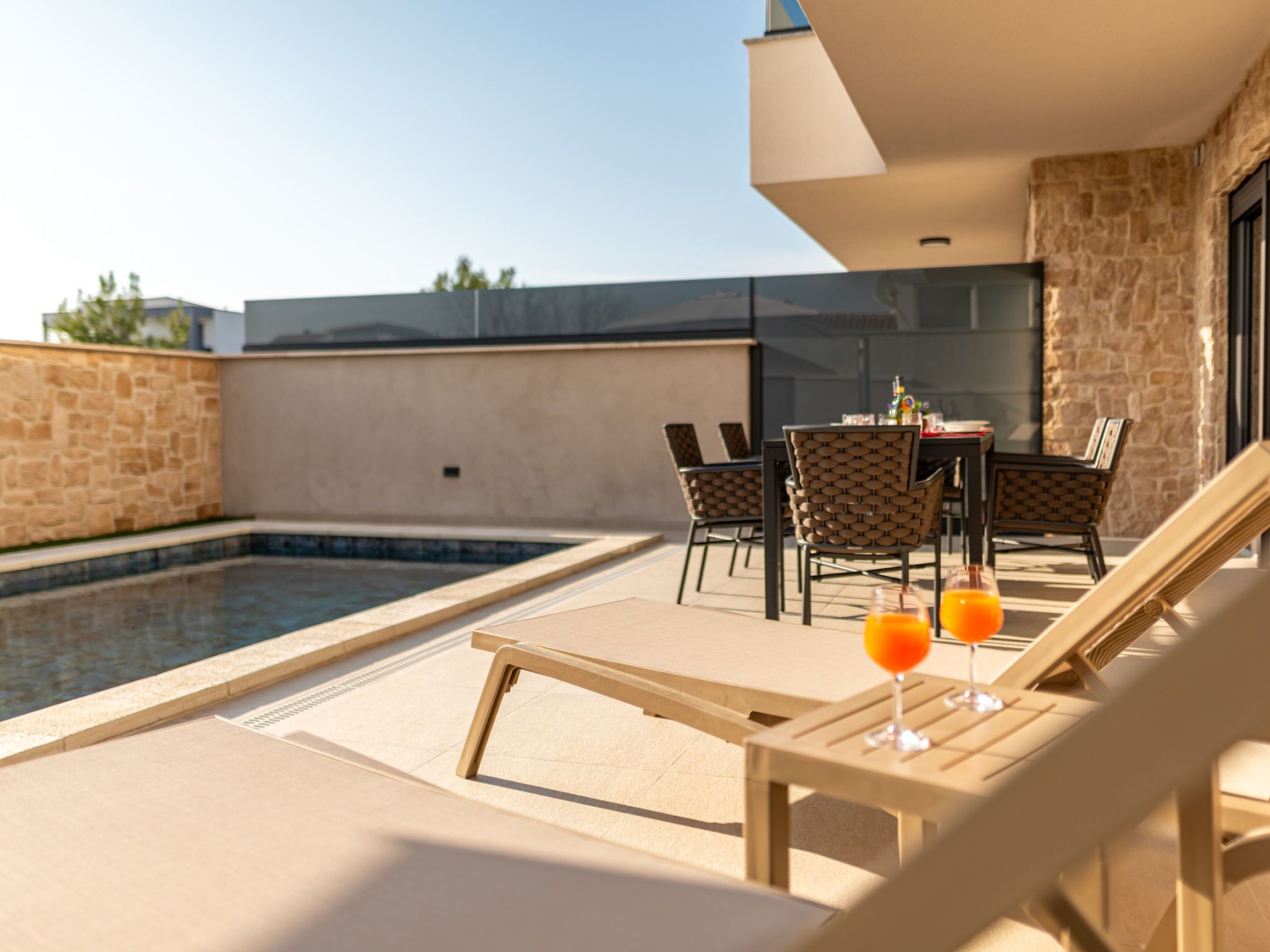 A poolside area with lounge chairs and a table, a small pool, and a stone wall.