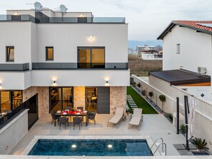 Ein modernes, zweistöckiges Haus mit Swimmingpool, Essbereich im Freien und einer Steinsäule.