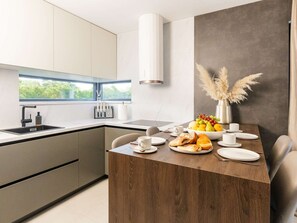 A modern kitchen with a dining area, featuring a built-in stove, a window with a view, and a table set with breakfast. - Luxury Villa Positiva with heated pool by Interhome (Vir)