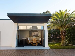 A modern house with a patio area featuring a dining table and chairs, a large window, and a palm tree in the background. - Luxury Villa Positiva with heated pool by Interhome (Vir)