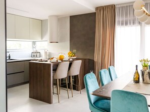 Une cuisine moderne dotée d’un îlot central, d’un coin repas avec des chaises de couleur turquoise et d’une grande fenêtre agrémentée de rideaux.