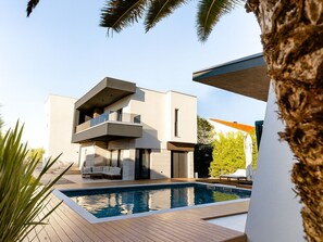 A modern two-story house with a swimming pool, outdoor furniture, and a palm tree. - Luxury Villa Positiva with heated pool by Interhome (Vir)