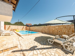 Ein Poolbereich mit Steinböden, Liegestühlen und blauem Himmel.